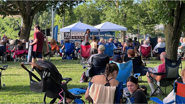 A view of the two white suncovers and the jazz band as it plays at sunset.  In the foreground, families with children enjoy the music.