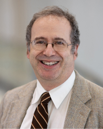 Dr. Ronald C. Samuels, MD, MPH. He smiles toward the camera, wearing a white shirt, maroon tie,  tan jacket and glasses.