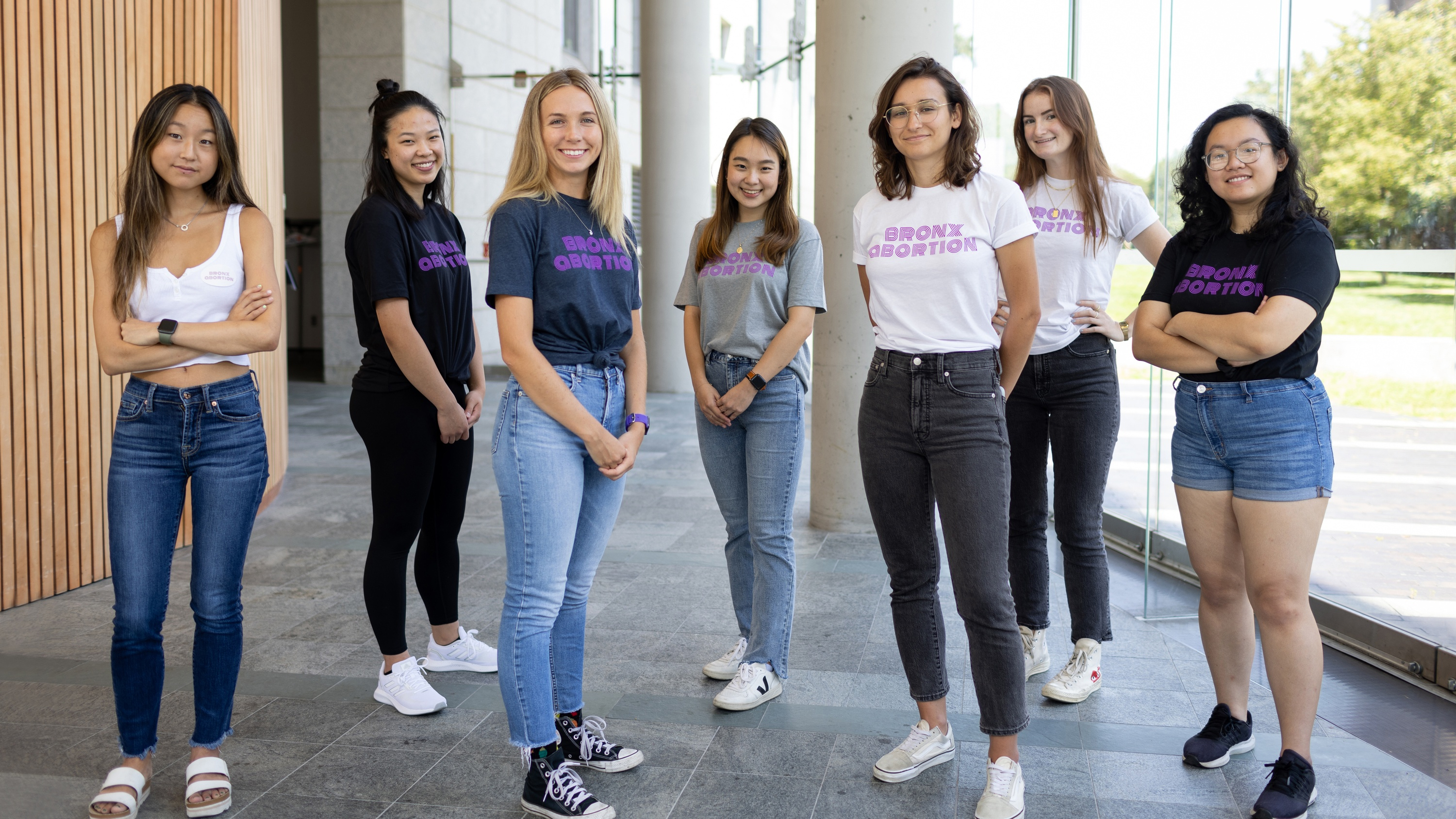 A group of seven students in jeans and t-shirts smile toward the camera.  The shirts read "Bronx Abortion".