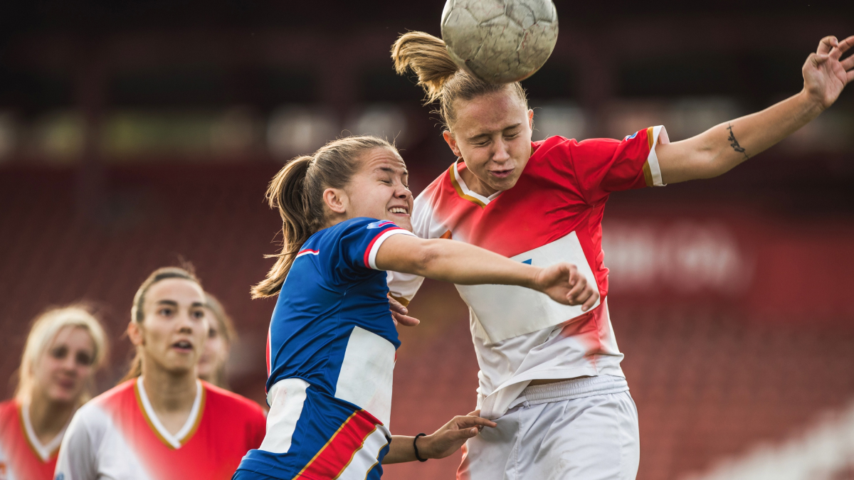 A soccer player heads the ball away from a charging opponent.