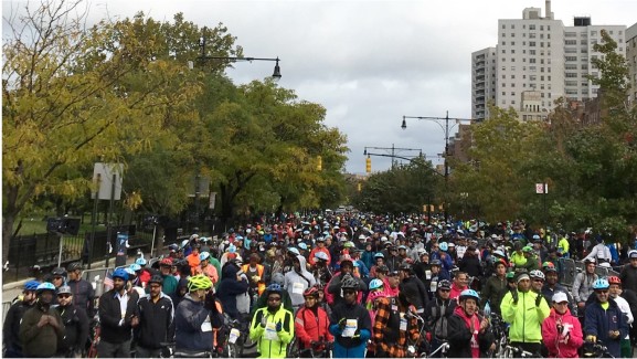 A crowd of races and onlookers are gathered in the street for the Tour de Bronx.