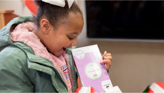 A child unwraps a package with a huge smile on her face.