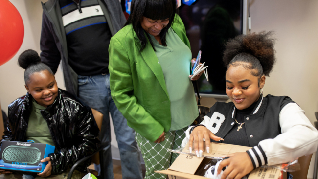 Kids open their gifts while an adult looks on. Everyone is smiling.