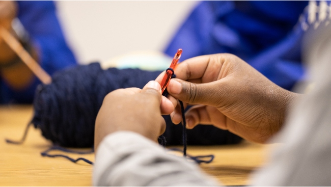 A closeup of hands working a crochet needle and navy blue yarn.