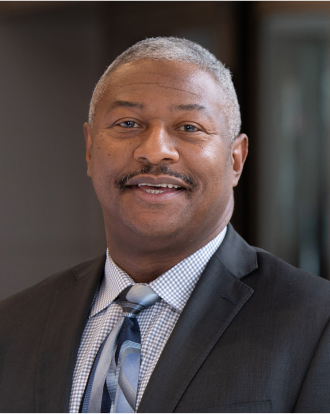 Robert L. Plummer dressed in a dark gray suit with a blue patterned tie.