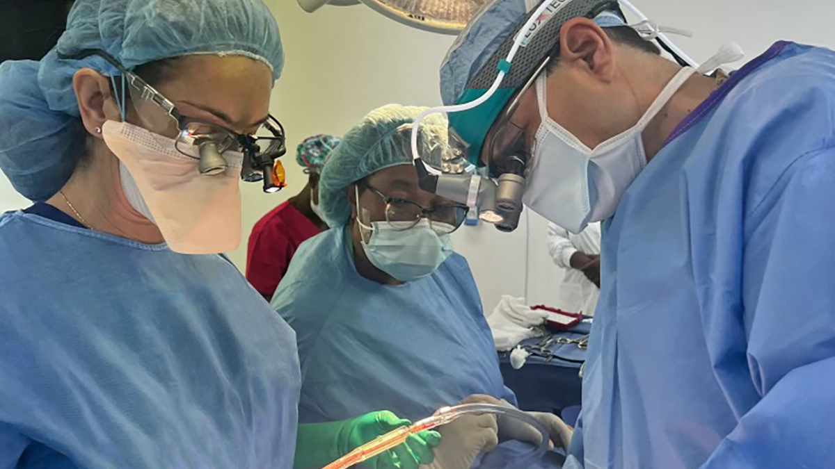 A group of three doctors in scrubs, masks, bonnets and gloves working on something.