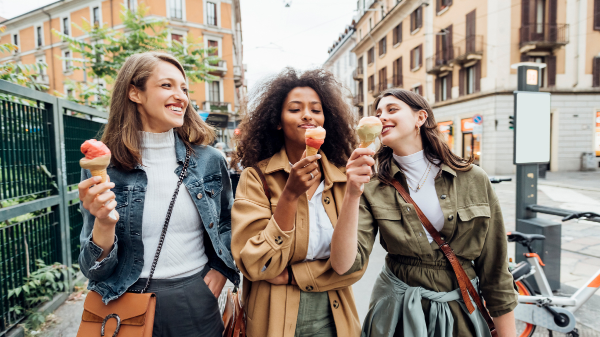 Three women walking down the street enjoying ice cream cones.