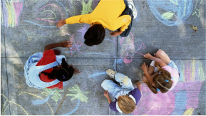 A top down view of children drawing on pavement with sidewalk chalk.