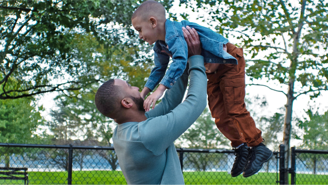 A parent holds their child up over their head as they both laugh and smile.