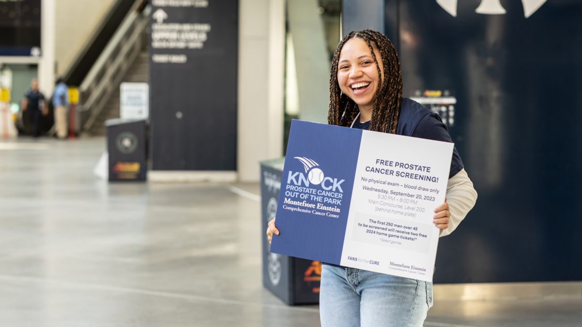 A smiling staffer holds up a sign for the "Knock Prostate Cancer out of the Park" event.