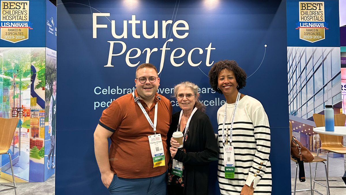 Three happy event participants smile in front of the Future Perfect event sign, in blue tones.