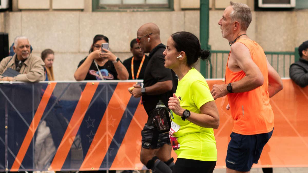 Marathoners run, being watched and cheered on by spectators behind a temporary fence.