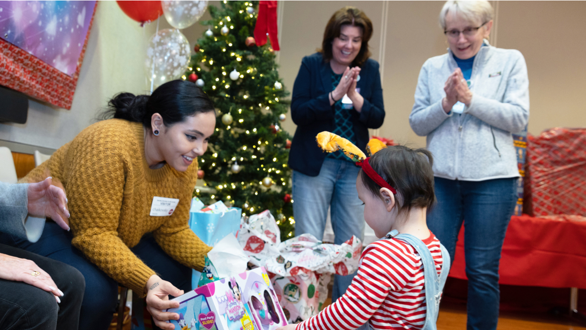 A child opens a gift as smiling adults look on.