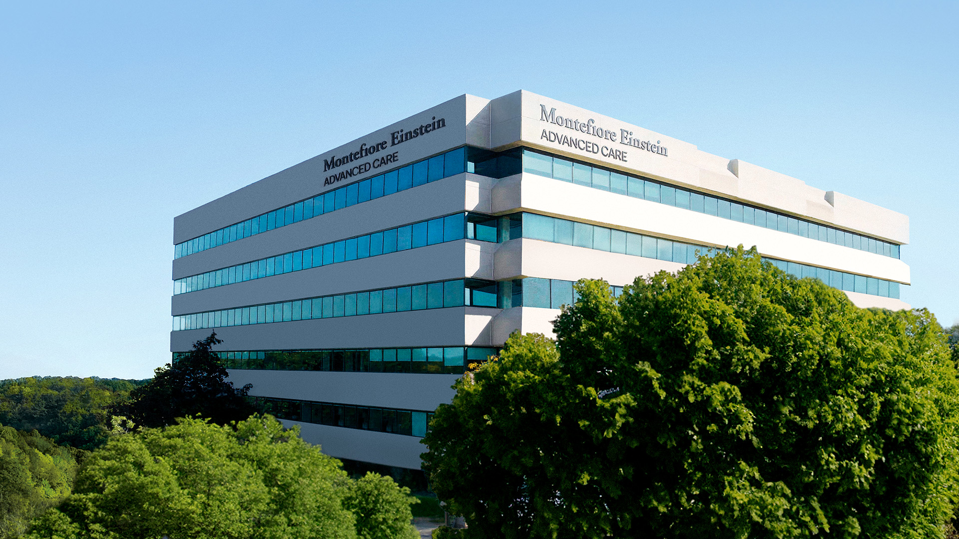 A view of the Montefiore Einstein Advanced Care building, bathed in sunlight on a clear summer day.