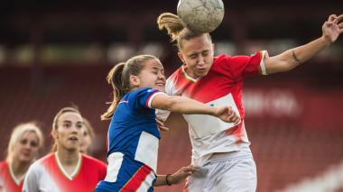 A soccer player heads the ball away from a charging opponent.