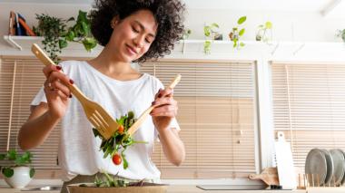 A smiling woman prepares mixed greens.