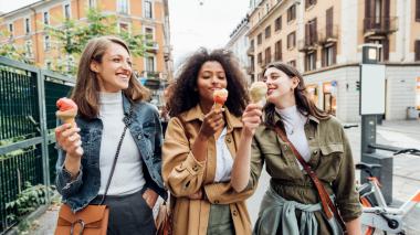 Three women walking down the street enjoying ice cream cones.