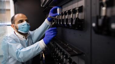 A masked scientist in protective gear runs a test.