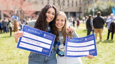 Two doctors smile and hold up their residency match cards.