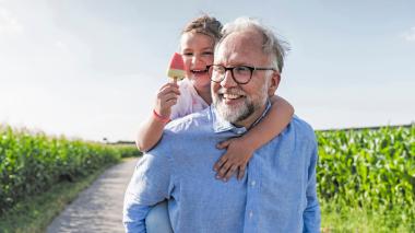 A happy man in a blue shirt carries a young child and their ice cream on his back.