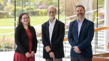 Three members of the Montefiore Einstein School of Medicine and Montefiore Health System team stand, smiling, in front of a glass wall with a view of a green courtyard.