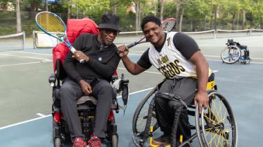 Two wheelchair athletes with tennis racquets smile for a picture.