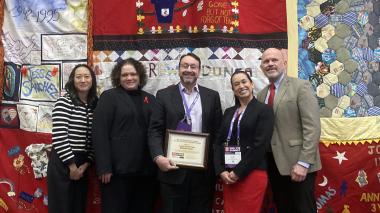 A group of doctors and staff stand in front of a quilt.