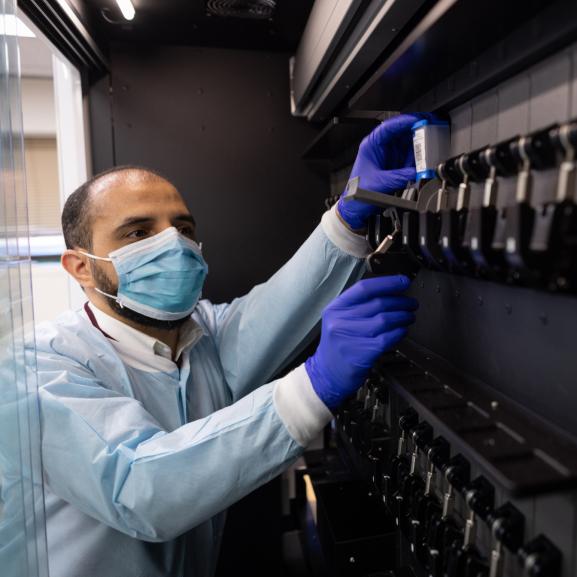 A masked scientist in protective gear runs a test.