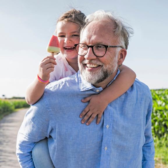 A happy man in a blue shirt carries a young child and their ice cream on his back.